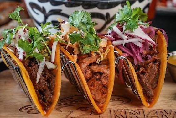 Kalaveras trio of tacos in front of a blue and white pattrned bowl