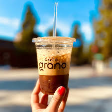 Cafe Grano coffee in a plastic cup with straw held in a hand painted with red fingernails