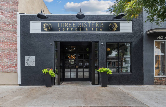 Three Sisters Coffee and Tea storefront, black building with sign and two potted plants