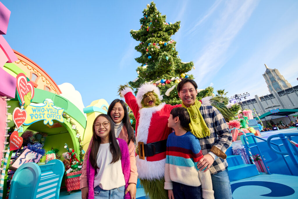 Grinch posing with a family of four in front of a Who Christmas tree for Grinchmas at USH