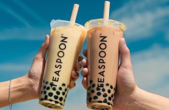 Two hands holding Teaspoon Boba drinks against a blue sky