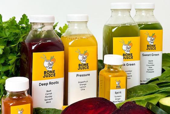 Row of bottled Bone Juice drinks of varying sizes with beets and green lettuce