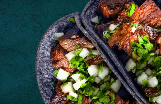 Two tacos with juicy grilled meat, onions, and cilantro on blue corn tortillas.