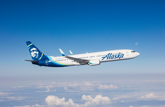 Alaska Airlines Boeing 737 flying above the clouds on a clear day.