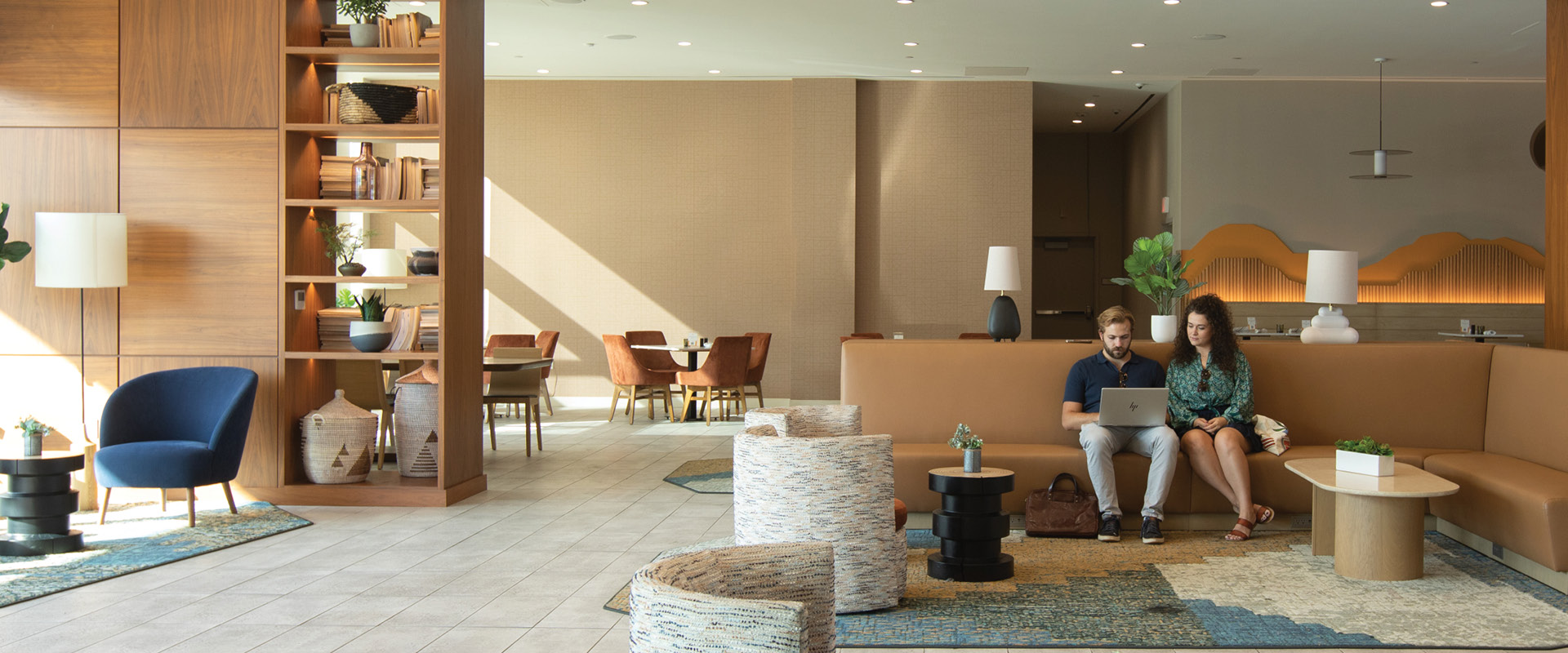 Modern hotel lobby with guests seated in a lounge area using a laptop.