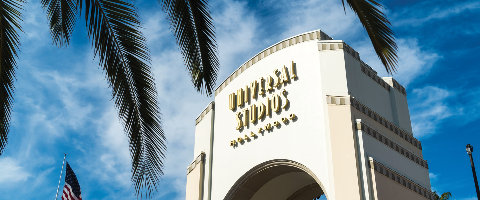 Universal Studios Hollywood entrance framed by palm trees beneath a bright blue sky.