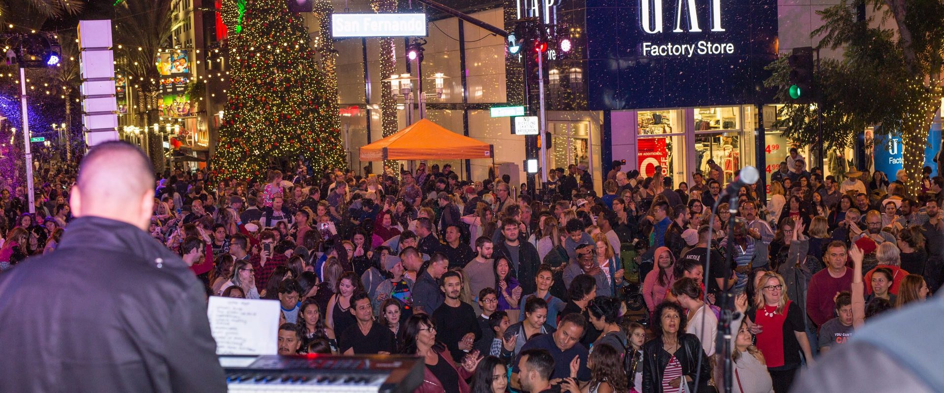 A packed evening crowd fills San Fernando Boulevard in front of a lit Christmas tree during the Burbank Winter Wine Walk