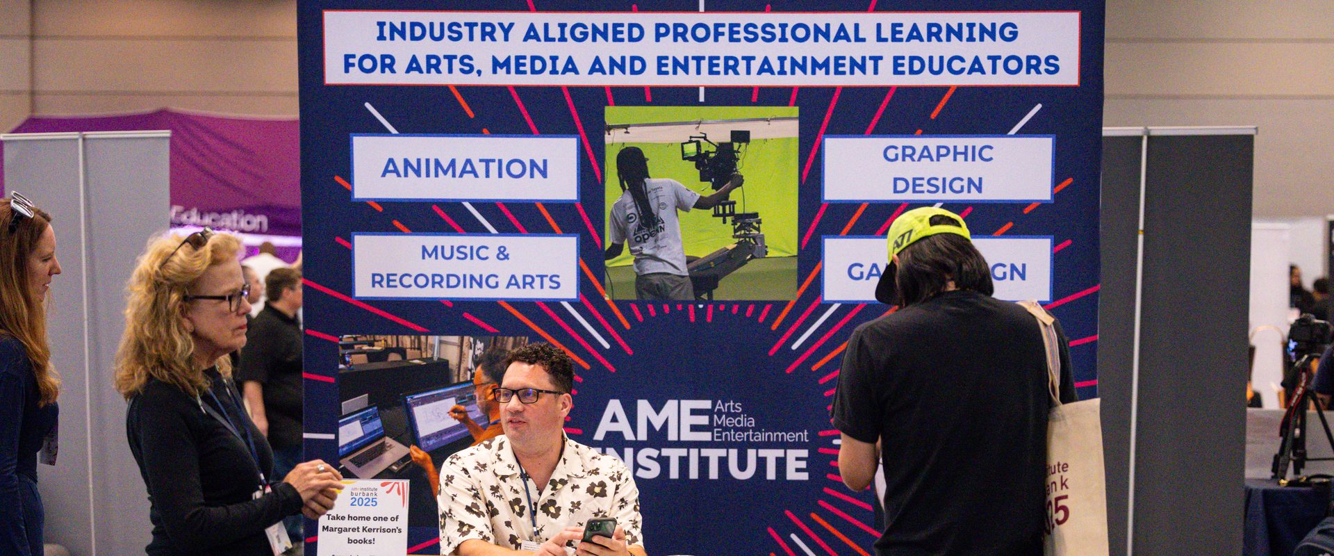 Educators visit the AME Institute booth under a banner reading "Industry Aligned Professional Learning for Arts, Media and Entertainment Educators"