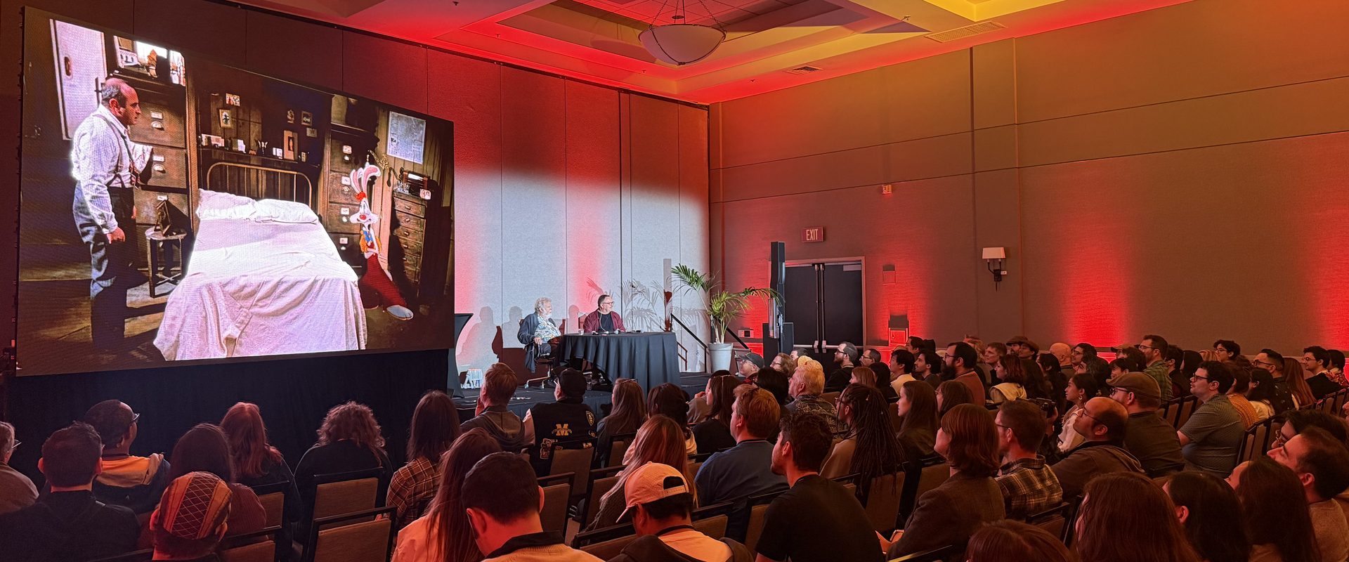 Packed ballroom audience watches a presentation on a large screen under red uplighting at CTN Animation Expo in Burbank