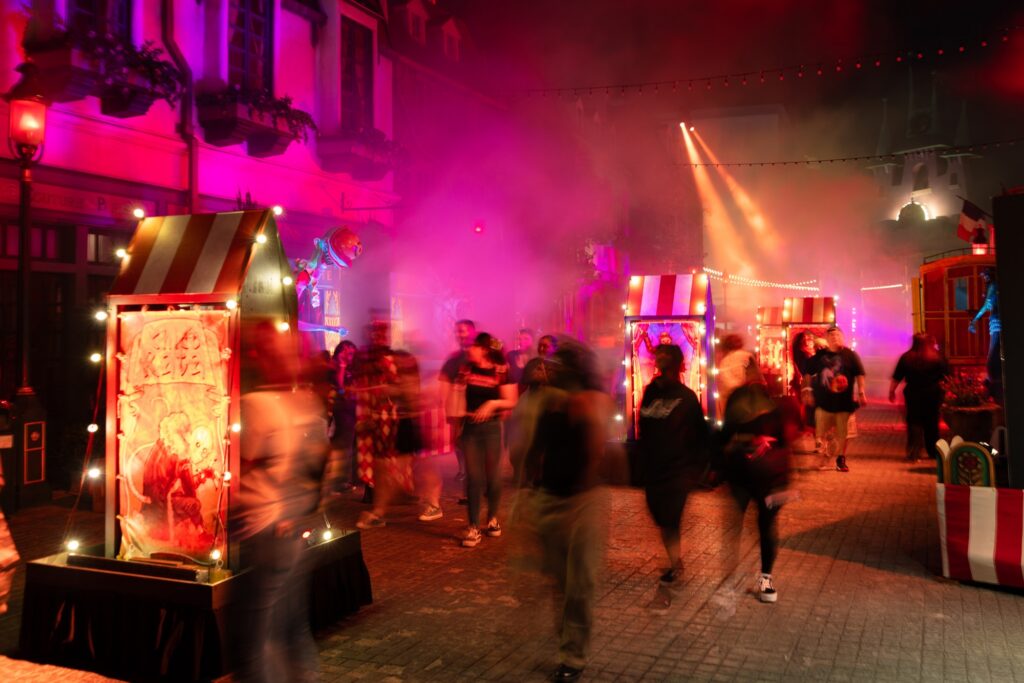 Crowds move through pink fog and carnival booths in the El Circo de la Muerte scare zone at Halloween Horror Nights