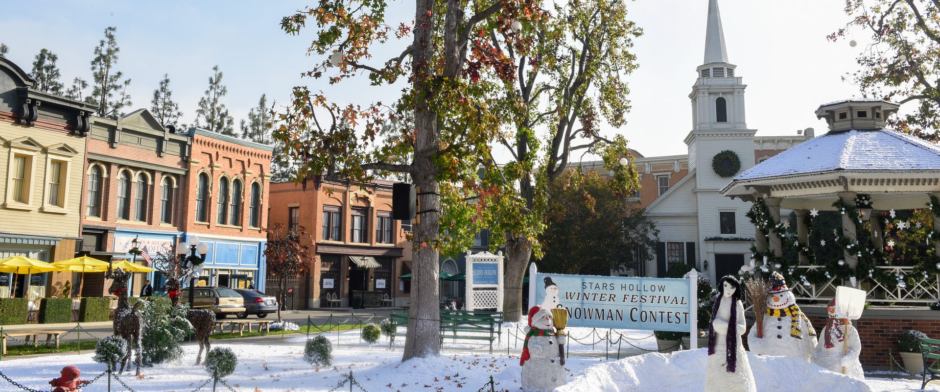 The Stars Hollow town square on the Warner Bros. backlot covered in snow, with snowmen, a Winter Festival sign, the gazebo and the white church