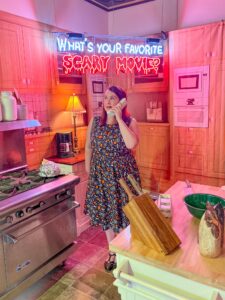 Visitor posing with a cordless phone under a neon "What's your favorite scary movie?" sign at the Mystic Museum in Burbank