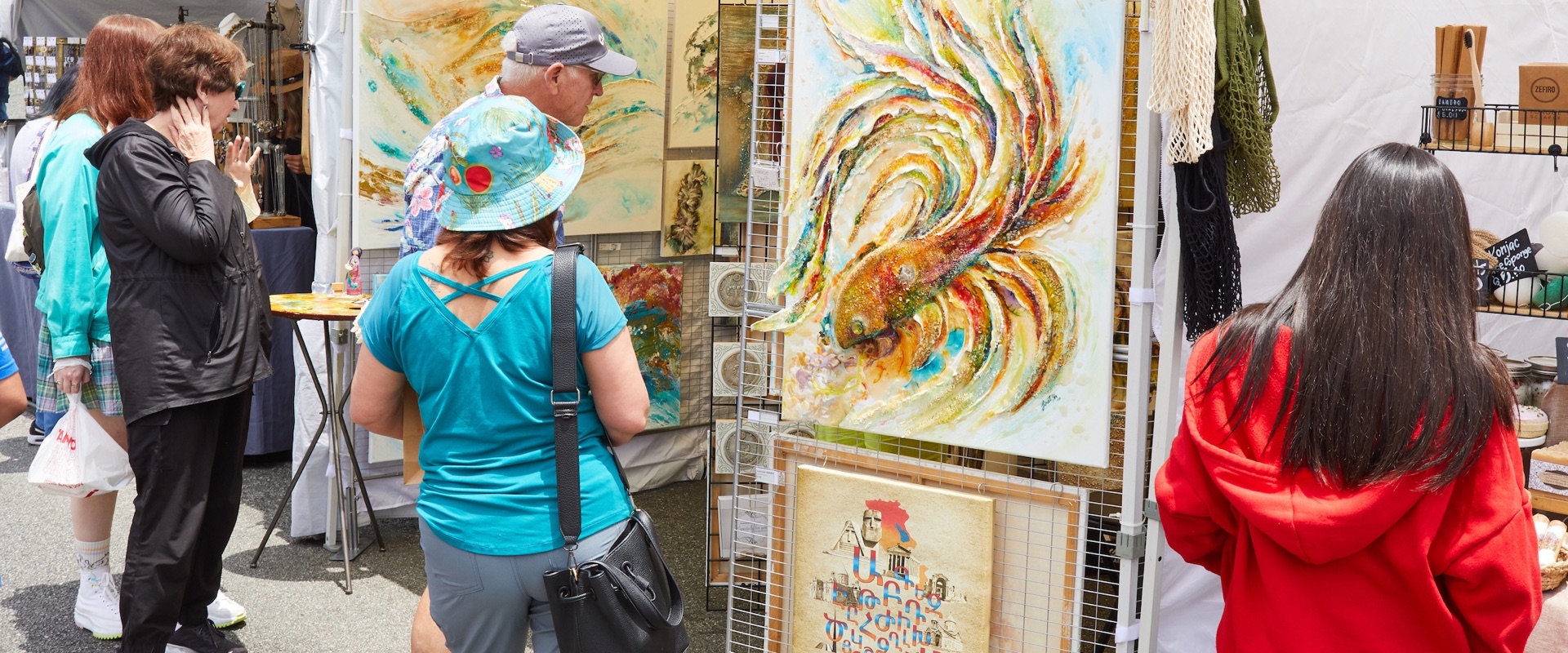 Shoppers in sun hats browse colorful paintings at an artist booth during the Downtown Burbank Summer Arts Festival