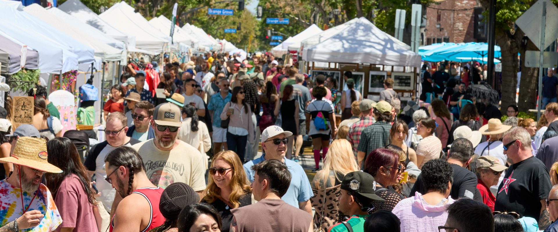 Crowds stroll between rows of white artisan tents on a tree-lined Downtown Burbank street at the Jackalope arts festival