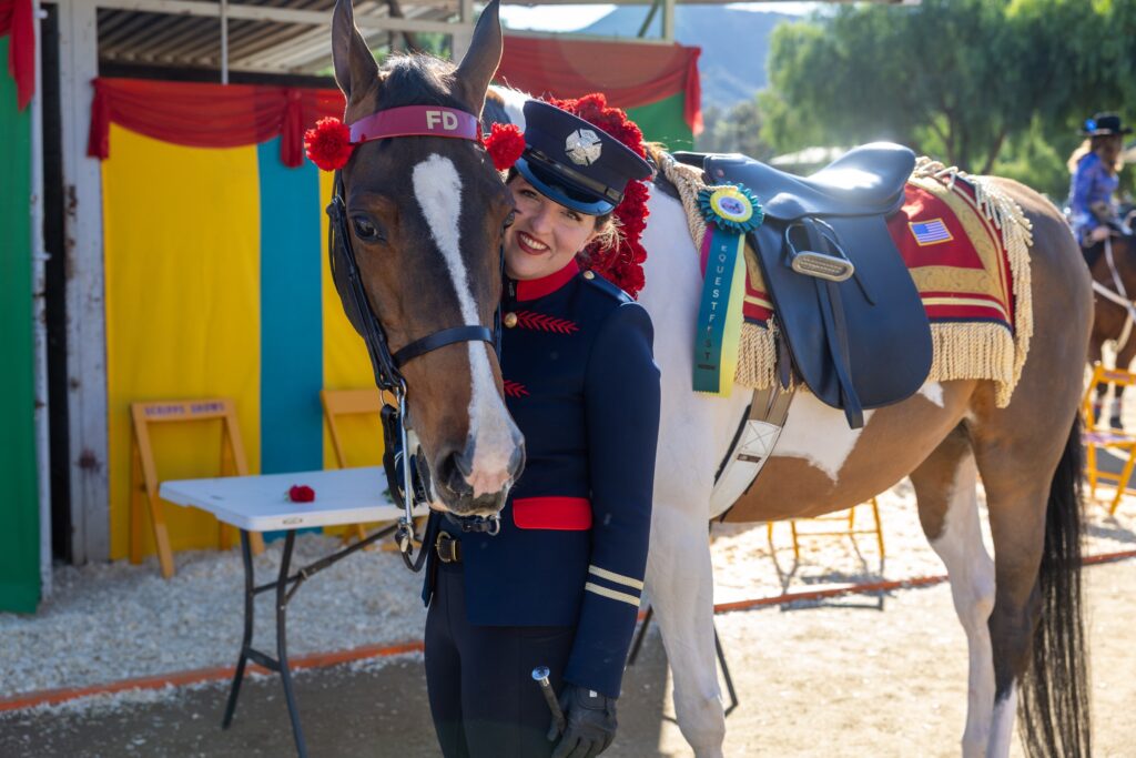 A rider in uniform beside a horse with a rose-trimmed bridle