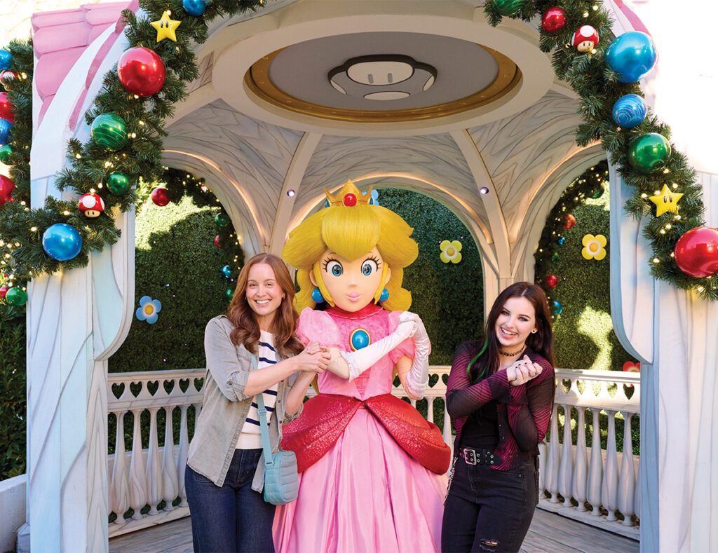 Two visitors with Princess Peach under a garland-trimmed gazebo at SUPER NINTENDO WORLD