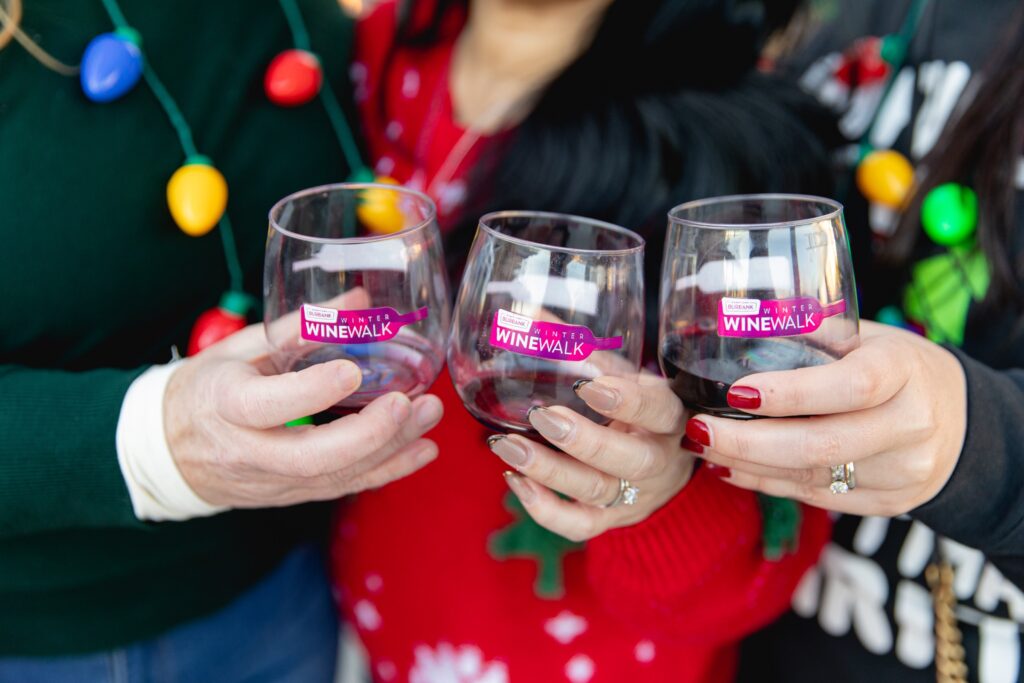 Friends in holiday-light necklaces toast with Winter Wine Walk glasses