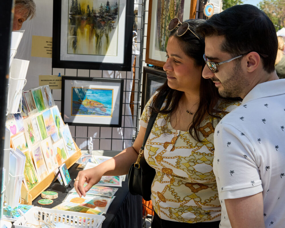 A couple browses paintings and prints at an artist's booth