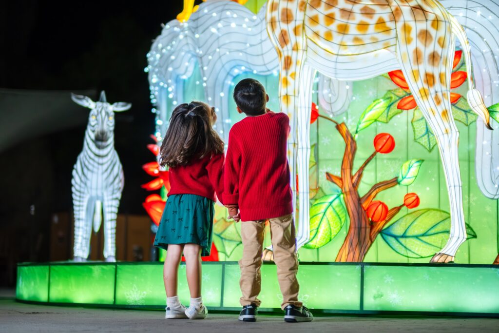 Two children looking up at glowing giraffe and zebra lanterns